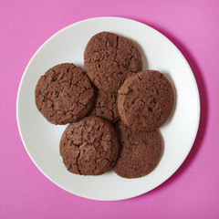 A plate of chocolate chunk cookies on a bright pink background