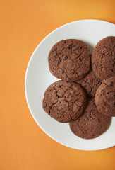 A plate of chocolate chunk cookies on a bright orange background
