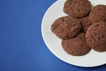 A plate full of chocolate chunk biscuits on a blue background forming a page border