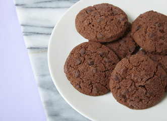 A plate full of chocolate chunk cookies on a pale purple background forming a page border