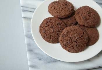 A plate full of chocolate chunk biscuits on a pale grey background forming a page border