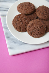A plate full of chocolate chunk cookies on a bright pink background forming a page border