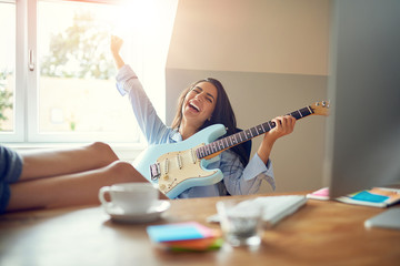 Laughing young woman with guitar and feet on table