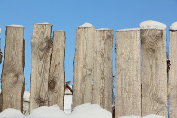 Old wooden fence against snow in the winter