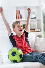 At home, a boy watching TV sport, he raises his arms in victory