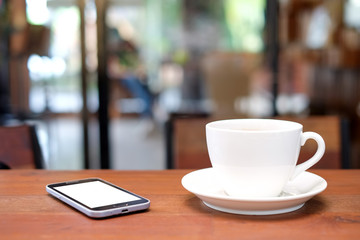 White coffee cup and smart phone on wooden table with blurred ca