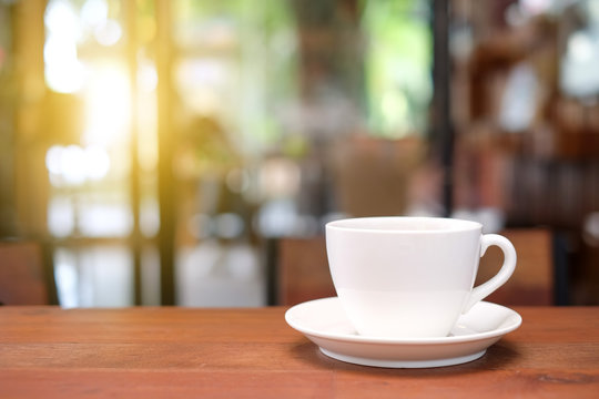 White coffee cup on wooden table with blurred cafe background.