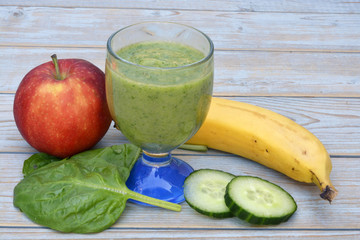 Glass of smoothie with fruit and green vegetable a banana ,cucumber and spinach on a wooden table background



