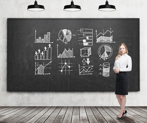 Smiling blond businesswoman with graphs on blackboard
