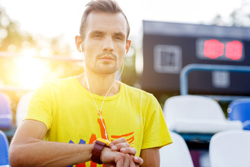 Athletic man in headphones and with clock in stadium