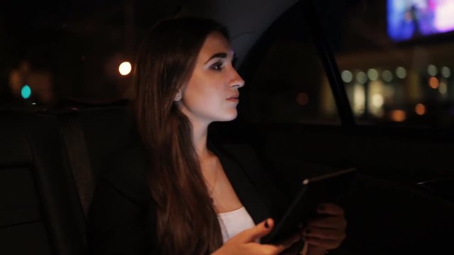 Beautiful girl riding in a taxi at night and read the messages on the tablet
