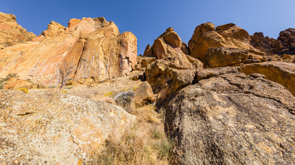 Unusual shaped rocks on the background of blue sky. The sheer rock walls. Beautiful landscape of yellow sharp cliffs. Dry yellow grass grows at the foot of cliffs. Smith Rock state park, Oregon