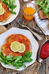 Pork schnitzel with organic arugula and lime on a old wooden background.