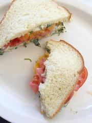 Partially-eaten sandwich of heirloom tomato and cilantro mayonnaise on white bread