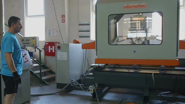 One part of the machine on the production line lowers down. A worker is regulating the process with a computer. Wide-angle shot.
