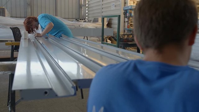 Two workers are each working on both ends of the long thin metal rods and are adjusting something. Close-up shot.
