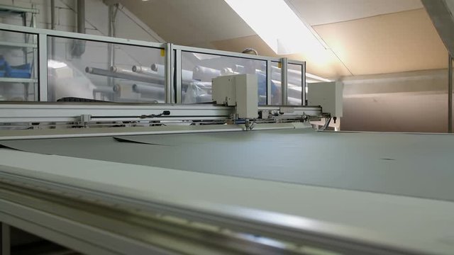 A machine is slowly moving on the production line and it is cutting fabric into two separate pieces. Wide-angle shot.
