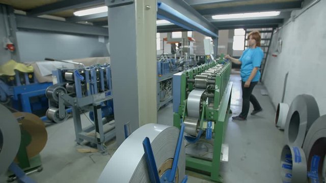 A woman who is working behind a production line in the factory is pushing a button on the screen and then she takes a step back. Wide-angle shot.
