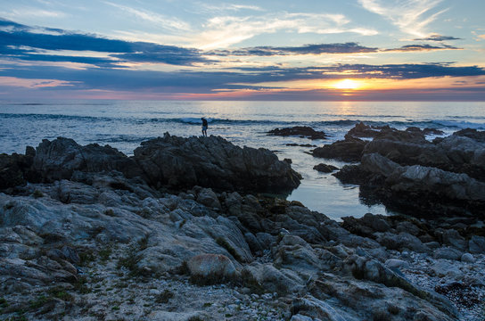 Lone person standing on rocks  with ocean sunset