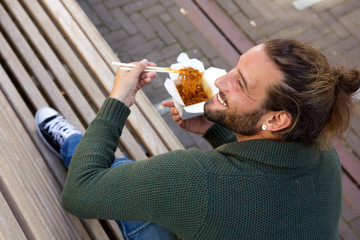 Smiling man eating chinese food on bench