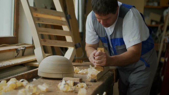 A carpenter is wood shaving in his workshop at home. He is working with a plane on a wooden background. Close-up shot.
