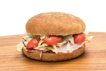 Wholemeal hamburger bun with ham, salad, tomatoes and mayonnaise on a wooden plate with white background 
