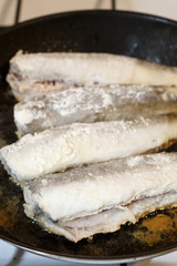 Fried hake fish fillet in a frying pan