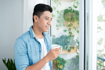 Thoughtful asian man looking out the window in bedroom at home