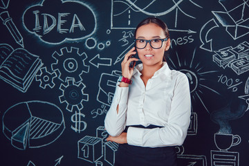 Portrait of a asian business woman in glasses on dark background with pictures and making phone call