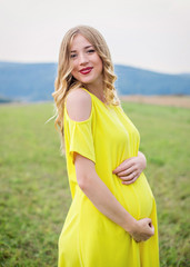 Beautiful pregnant woman in yellow dress relaxing outside at nature
