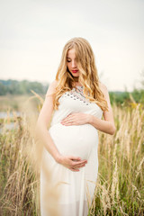 Fototapeta na wymiar Portrait of a young beautiful pregnant woman with long blond hair in a white dress