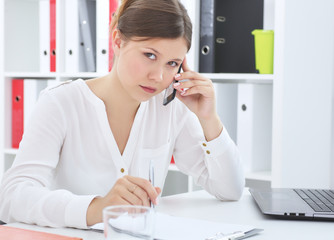 Beautiful young business woman sitting at office desk and talking on cell phone.