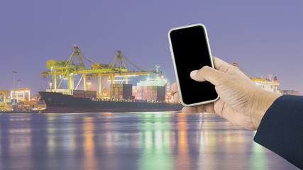 Hand holding phone over Container Cargo freight ship with workin