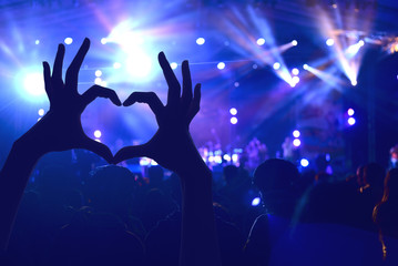 Festival crowd raising hands in music concert front of bright st