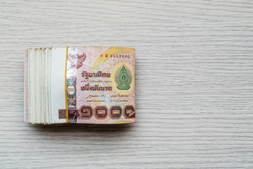 Stack of thousand bath Thai money on wooden table with copy space