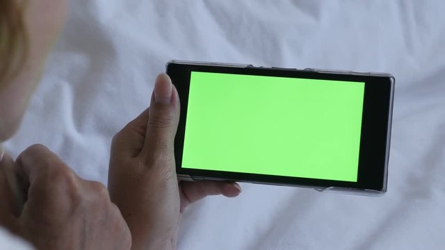 Chroma key greenscreen smart gadget in woman hands 4K 2160p 30fps UHD footage - Female relaxing in bed on mobile phone with green screen display 3840X2160 UltraHD video 