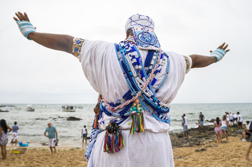 A Brazilian candomble priest performs a blessing at the Festival of Yemanja in traditional blue and white robes with colorful beads on the beach at Rio Vermelho in Salvador, Bahia, Brazil