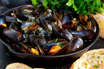 Boiled mussels in iron pan cooking dish. with herbs, butter, lime, parsley, garlic and fresh bread.