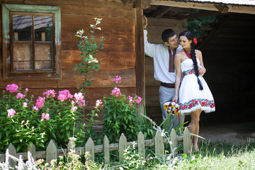 Fototapeta premium Groom hugs bride from behind while leaning to the ethnic house