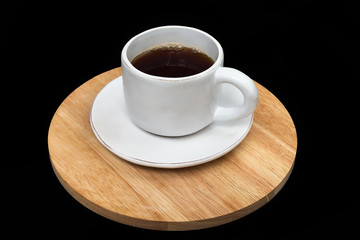 Filled white cup and sauser stading on a wooden stand isolated on black background. Ceramic white...