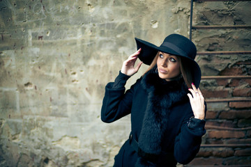Woman touches her black hat while posing in winter coat