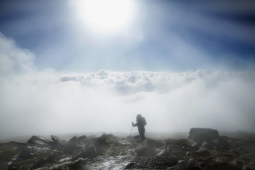 Mountaineer reaches the top of mountain in fog and autumn morning sun