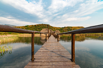Wooden bridge over dam, leading to thatched building, alongside a park near Champagne Castle, in the Drakensberg.