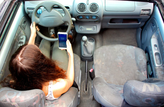 Junge Frau mit Handy am Steuer eines Autos
