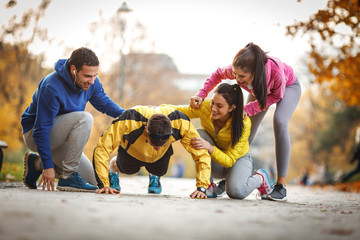Group of friends doing push-ups at the park and making fun,smiling and laughing.Autumn season.
