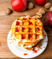 Autumn belgian waffles with apple jam, next to apples and nuts. On a wooden table.