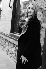 Black and white photo. Beautiful young blonde woman walking on the street. Dressed in a black coat and a warm knit sweater.