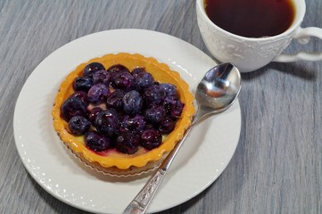 Tasty tart with blueberry and hot black tea in a white cup
