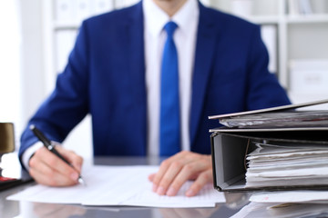 Binders with papers are waiting to be processed with businessman back in blur. Accounting planning budget, audit, insurance  and business concept