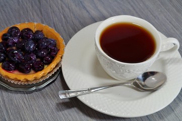 Tasty tart with blueberry and hot black tea in a white cup
